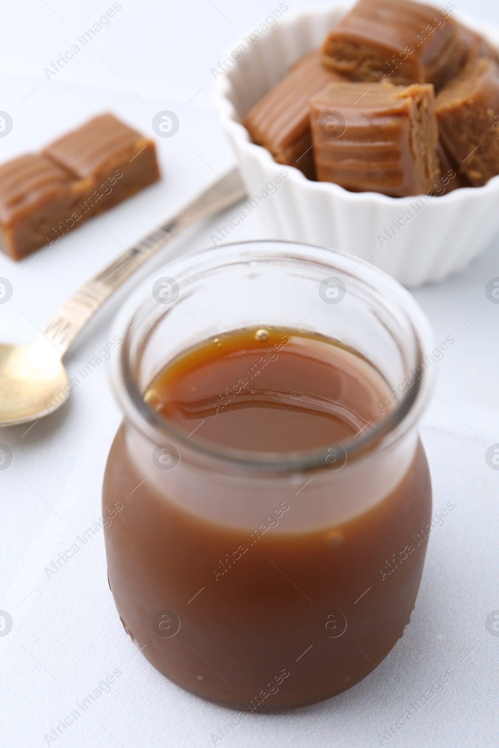 Photo of Tasty caramel sauce in jar and candies on white table, closeup