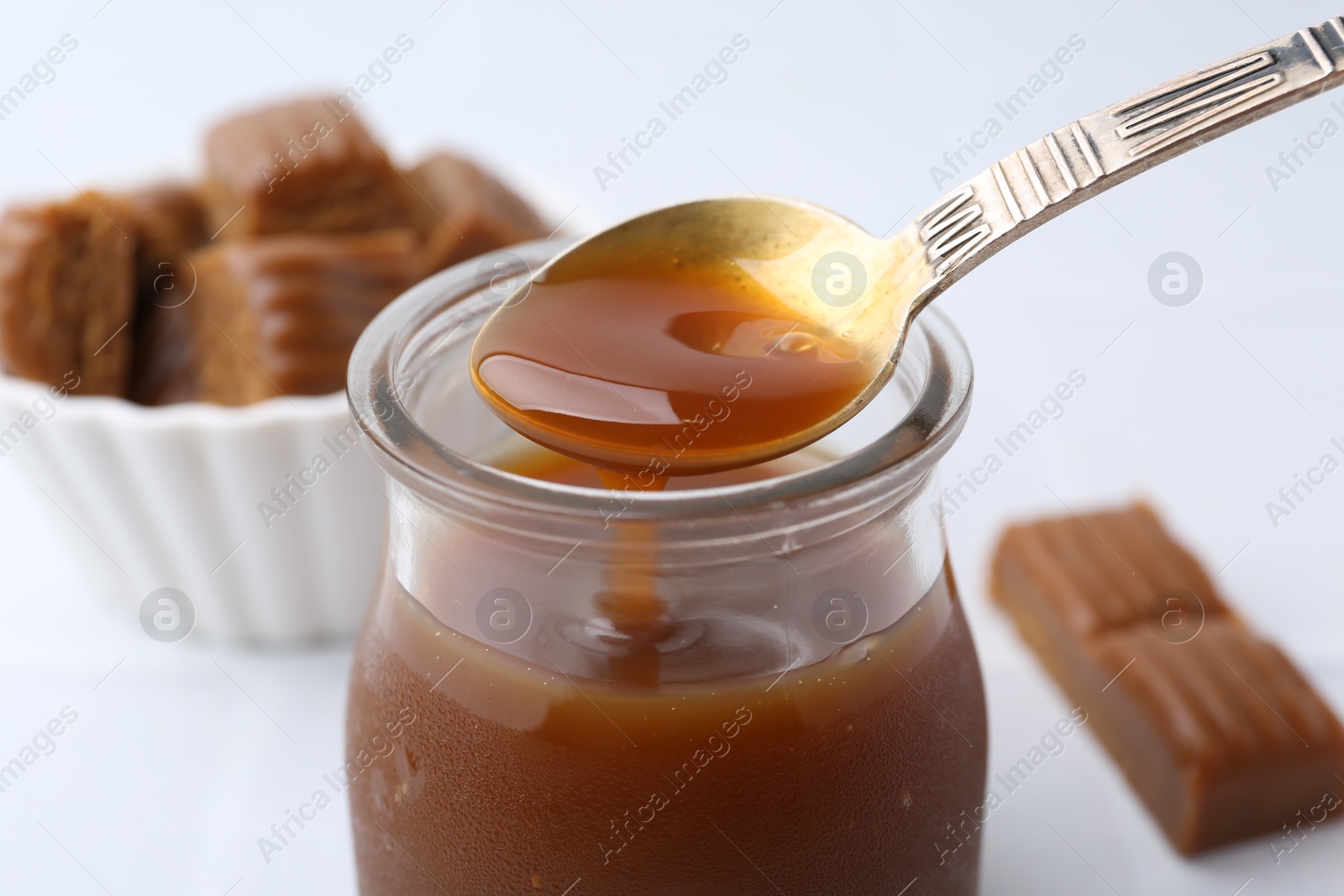 Photo of Taking tasty caramel sauce from jar with spoon at light table, closeup