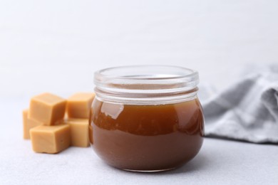 Tasty caramel sauce in jar and candies on light table, closeup