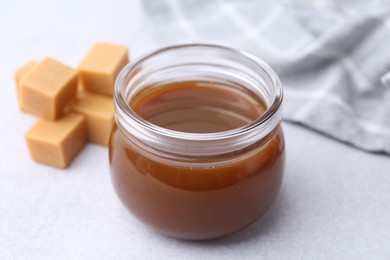 Photo of Tasty caramel sauce in jar and candies on light table, closeup