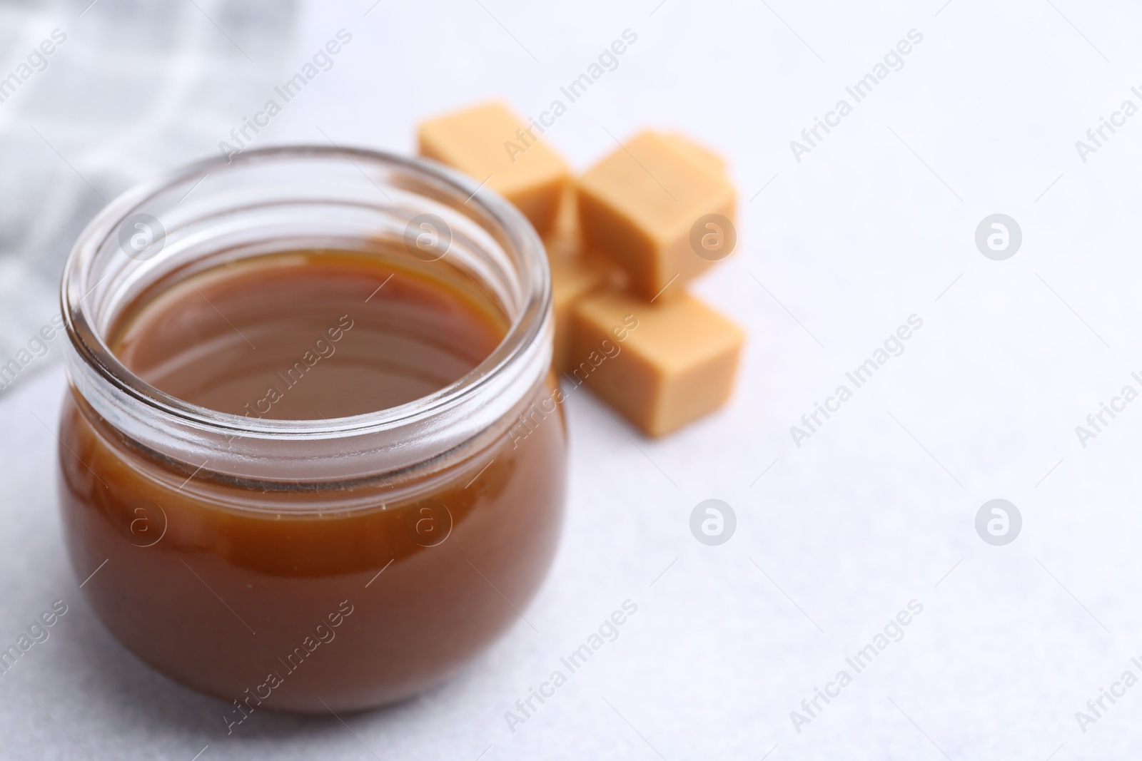 Photo of Tasty caramel sauce in jar and candies on light table, closeup. Space for text