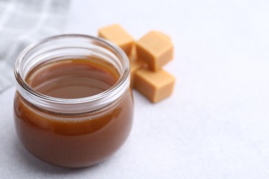 Photo of Tasty caramel sauce in jar and candies on light table, closeup. Space for text