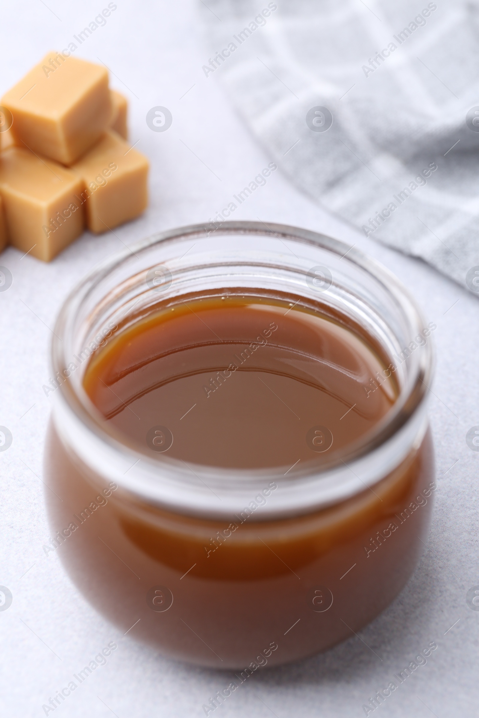 Photo of Tasty caramel sauce in jar and candies on light table, closeup