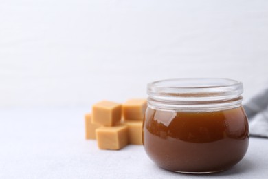 Tasty caramel sauce in jar and candies on light table, closeup. Space for text