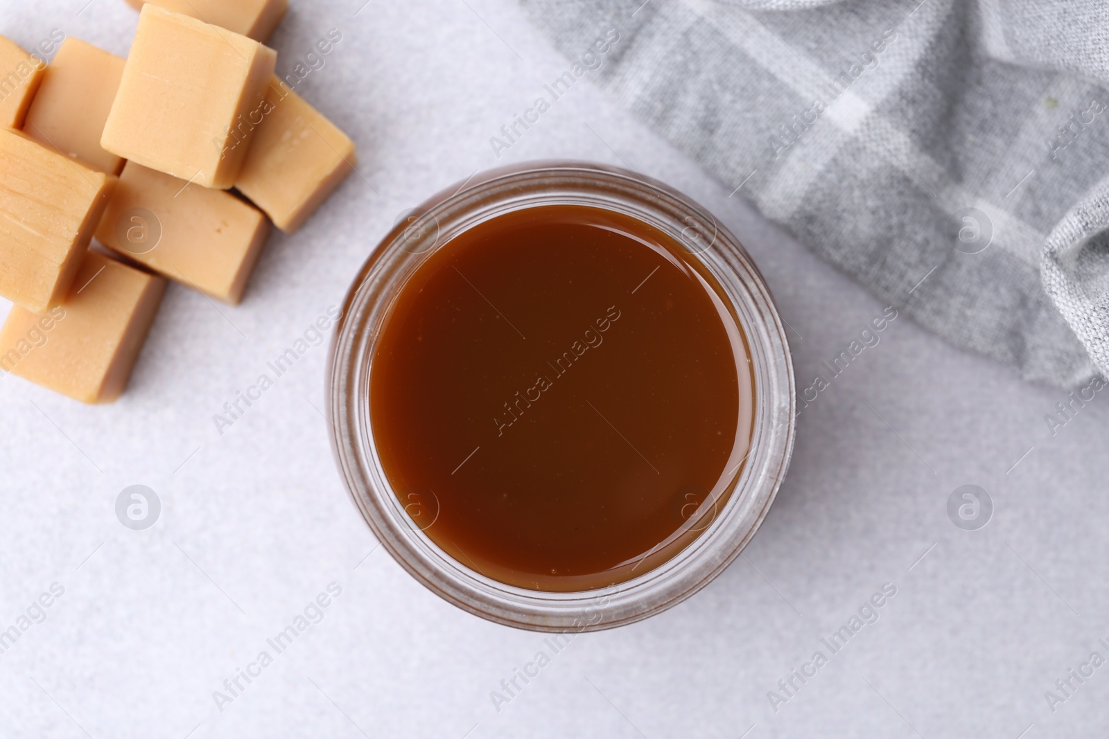 Photo of Tasty caramel sauce in jar and candies on light table, flat lay