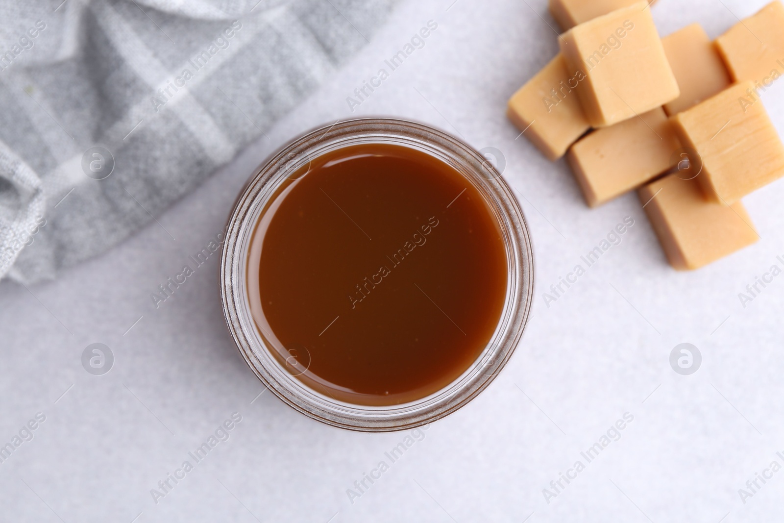 Photo of Tasty caramel sauce in jar and candies on light table, flat lay