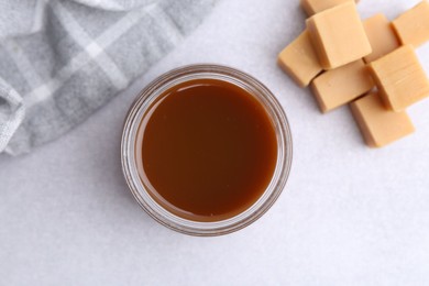 Tasty caramel sauce in jar and candies on light table, flat lay