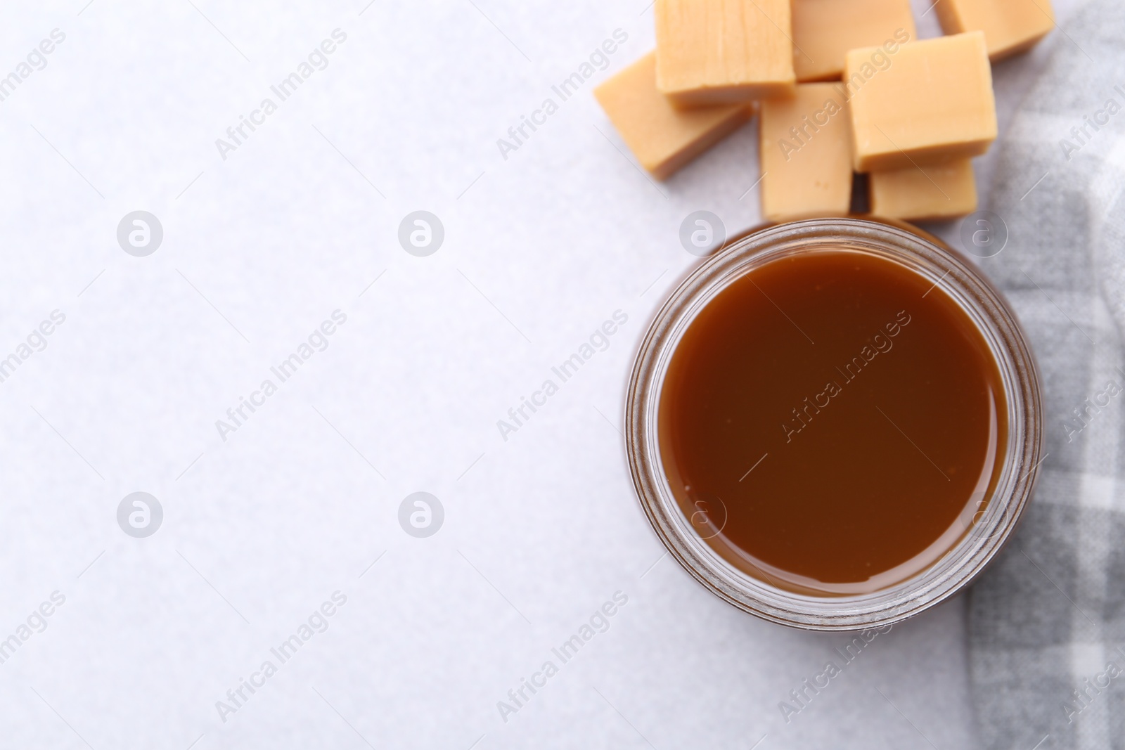 Photo of Tasty caramel sauce in jar and candies on light table, flat lay. Space for text