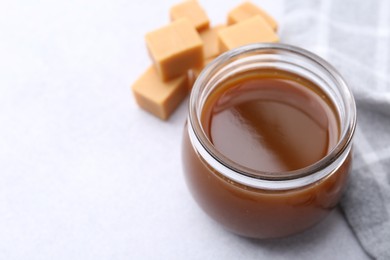 Photo of Tasty caramel sauce in jar and candies on light table, closeup. Space for text