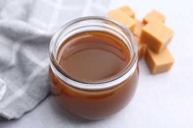 Photo of Tasty caramel sauce in jar and candies on light table, closeup