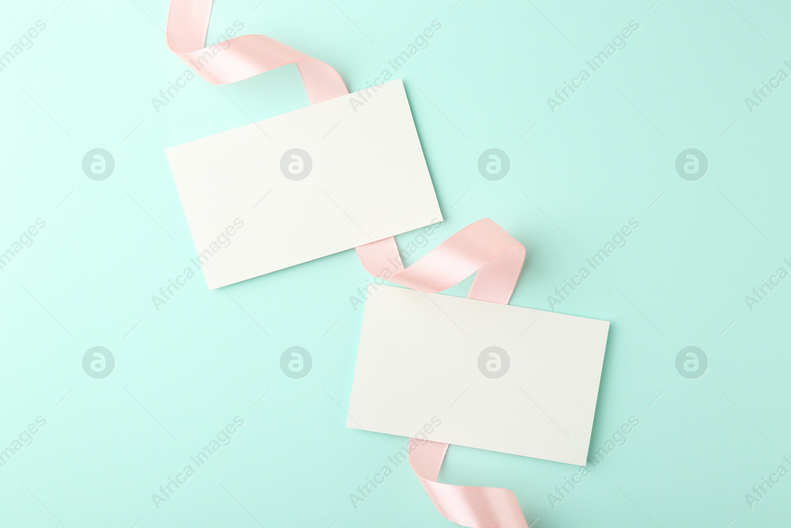 Photo of Blank cards and ribbons on turquoise background, flat lay