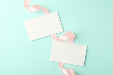 Photo of Blank cards and ribbons on turquoise background, flat lay