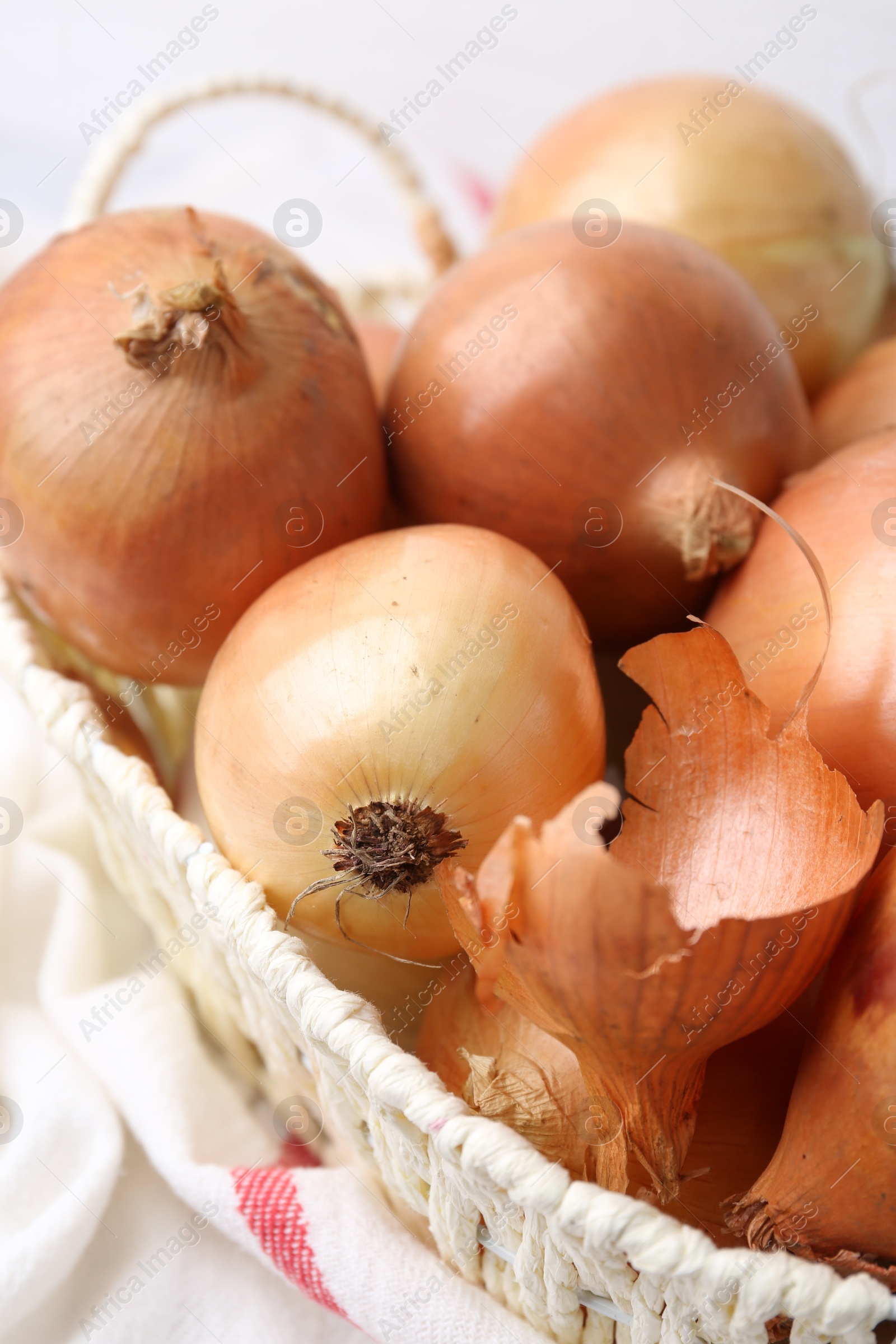 Photo of Fresh onions with peels in wicker basket on table, closeup