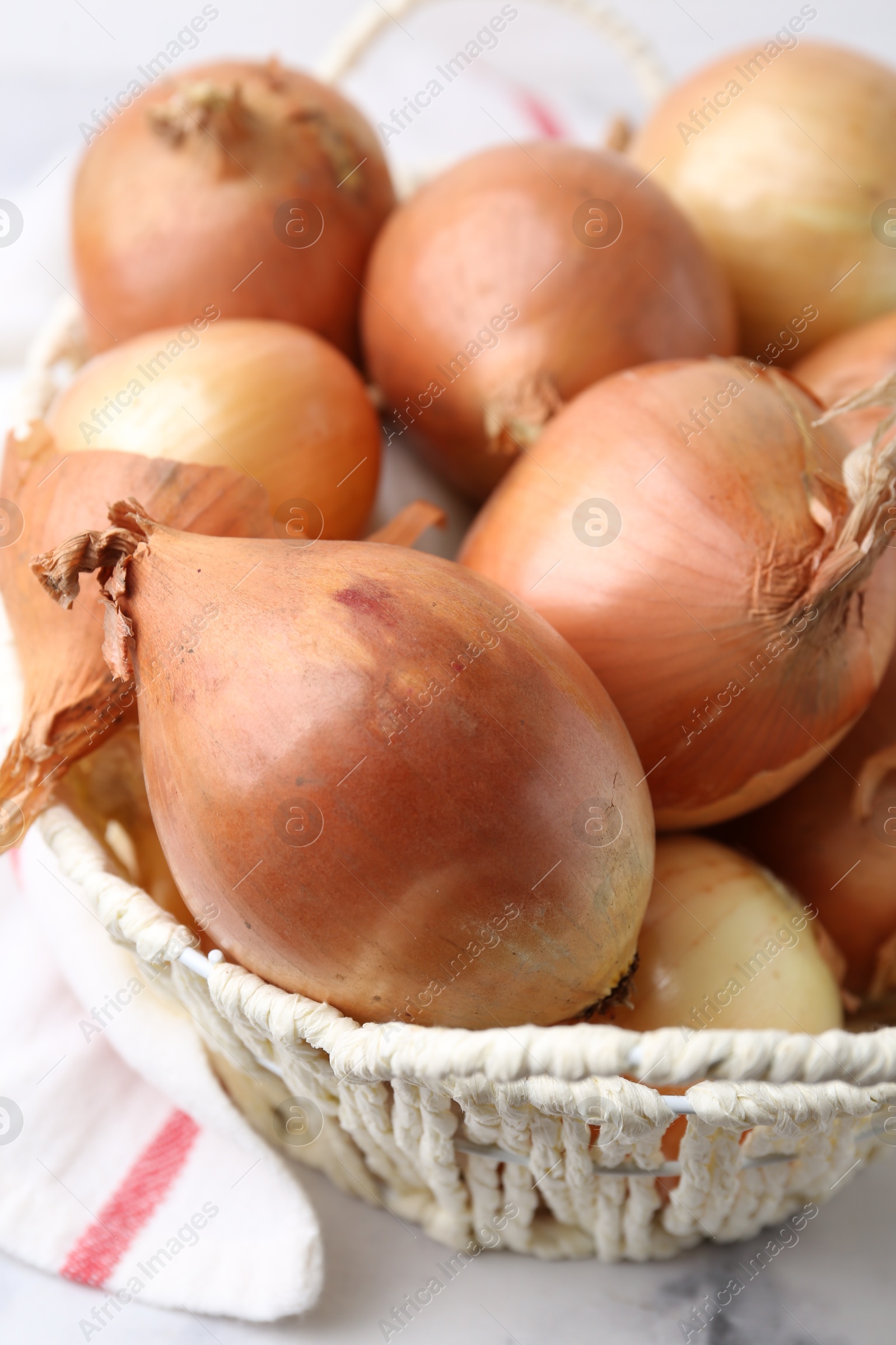 Photo of Fresh onions with peels in wicker basket on light table, closeup