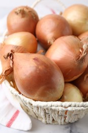 Photo of Fresh onions with peels in wicker basket on light table, closeup