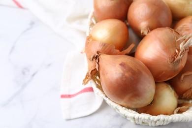 Photo of Fresh onions with peels in wicker basket on light marble table, above view. Space for text