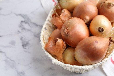 Photo of Fresh onions with peels in wicker basket on light marble table, above view. Space for text