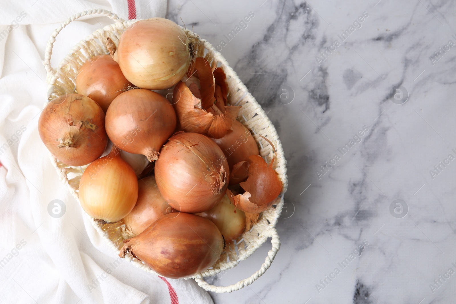 Photo of Fresh onions with peels in wicker basket on light marble table, top view. Space for text