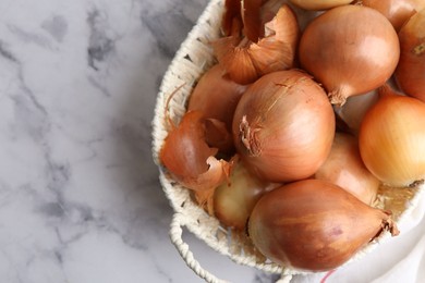 Photo of Fresh onions with peels in wicker basket on light marble table, top view. Space for text