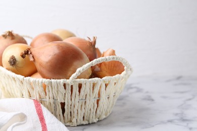 Fresh onions with peels in wicker basket on light marble table, closeup. Space for text