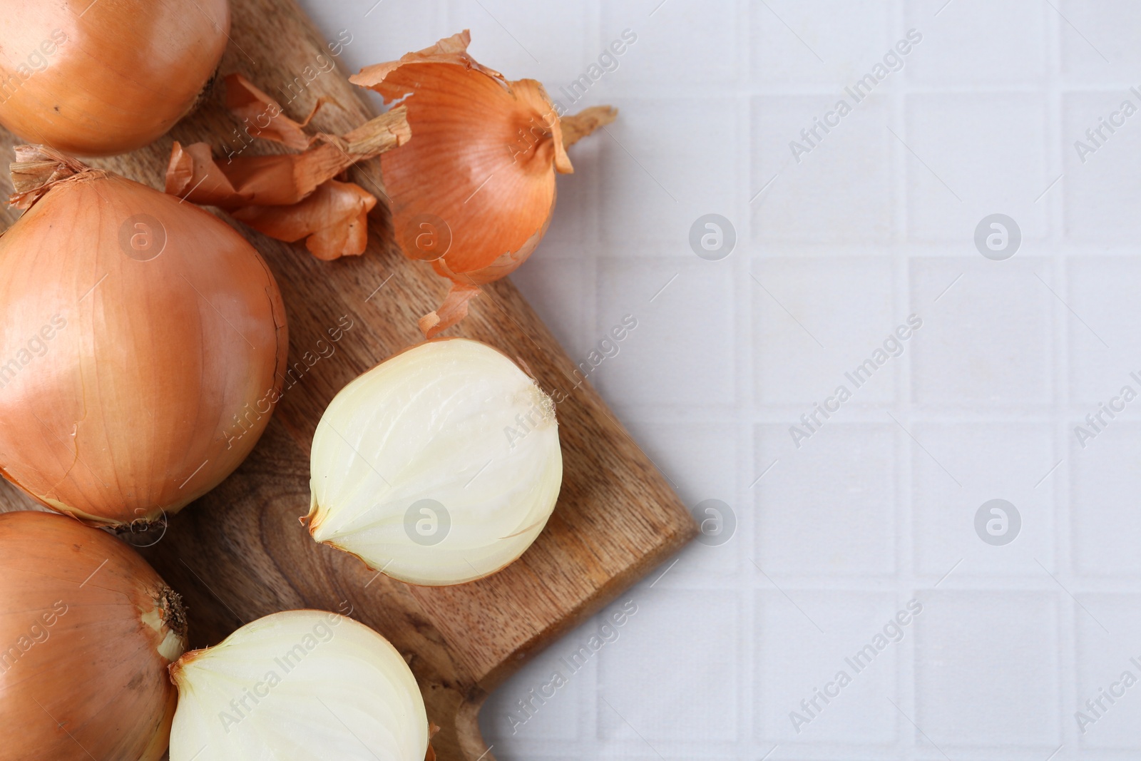 Photo of Fresh onions with peels on white tiled table, top view. Space for text