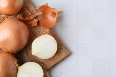 Fresh onions with peels on white tiled table, top view. Space for text