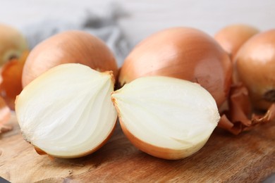 Fresh onions with peels on wooden board, closeup