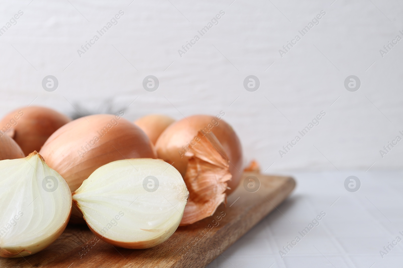 Photo of Fresh onions with peels on white tiled table, closeup. Space for text