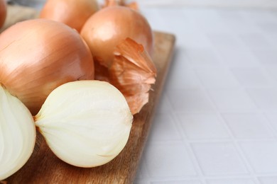 Photo of Fresh onions with peels on white tiled table, closeup. Space for text