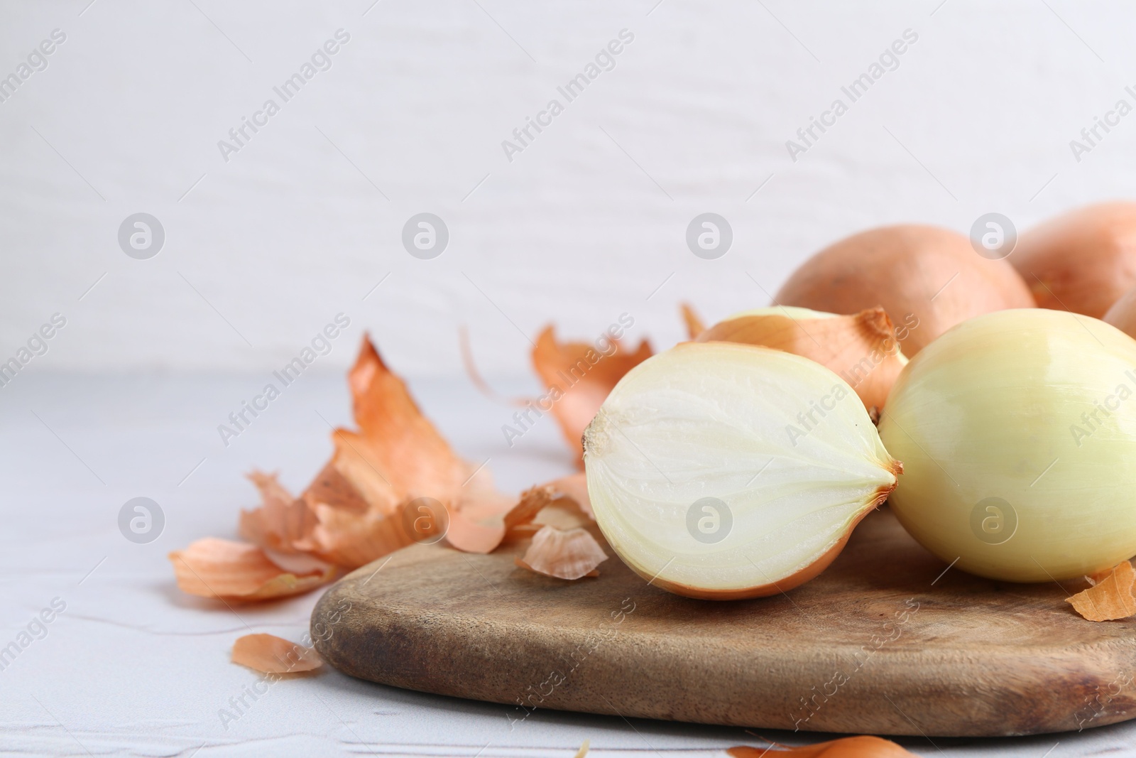 Photo of Fresh onions with peels on light textured table, closeup