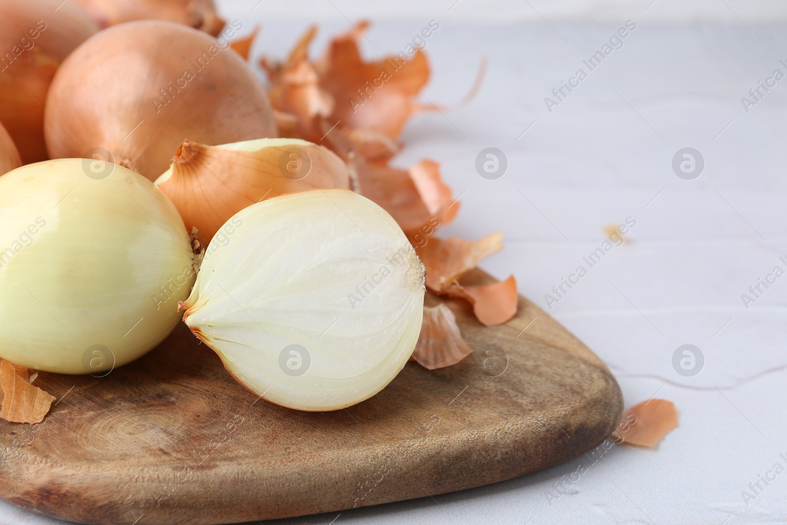 Photo of Fresh onions with peels on light textured table, closeup