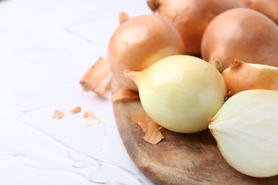 Photo of Fresh onions with peels on light textured table, closeup. Space for text