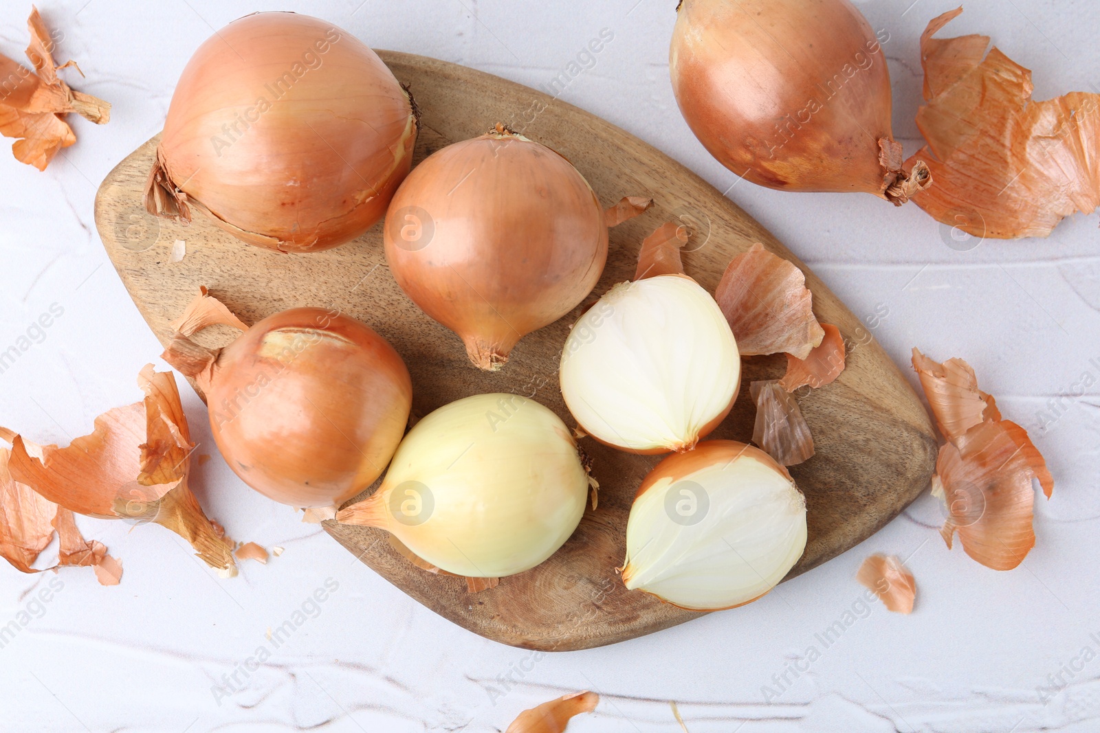 Photo of Fresh onions with peels on light textured table, top view