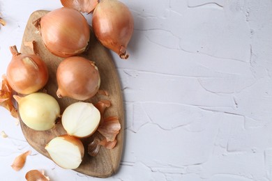 Photo of Fresh onions with peels on light textured table, top view. Space for text