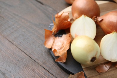 Photo of Fresh onions with peels on wooden table, closeup. Space for text