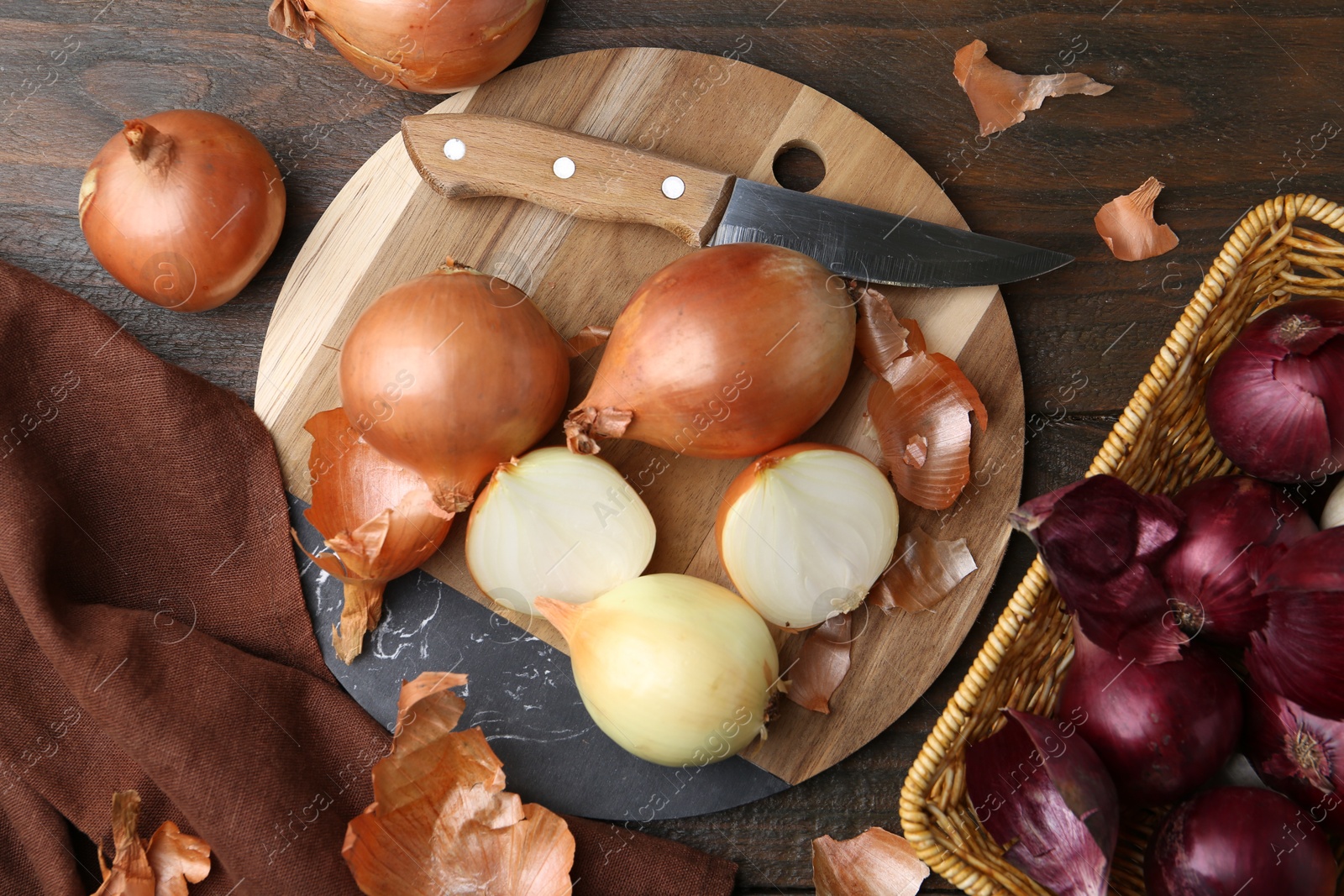 Photo of Fresh onions with peels and knife on wooden table, flat lay