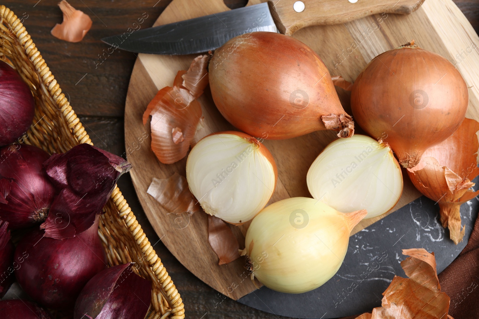 Photo of Fresh onions with peels and knife on wooden table, flat lay