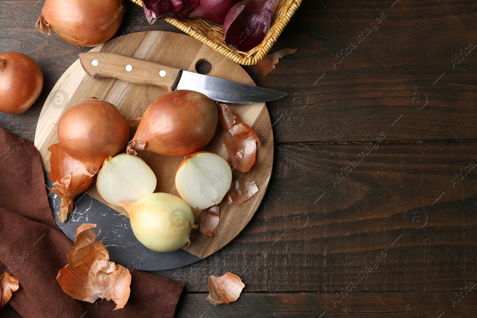 Photo of Fresh onions with peels and knife on wooden table, flat lay. Space for text