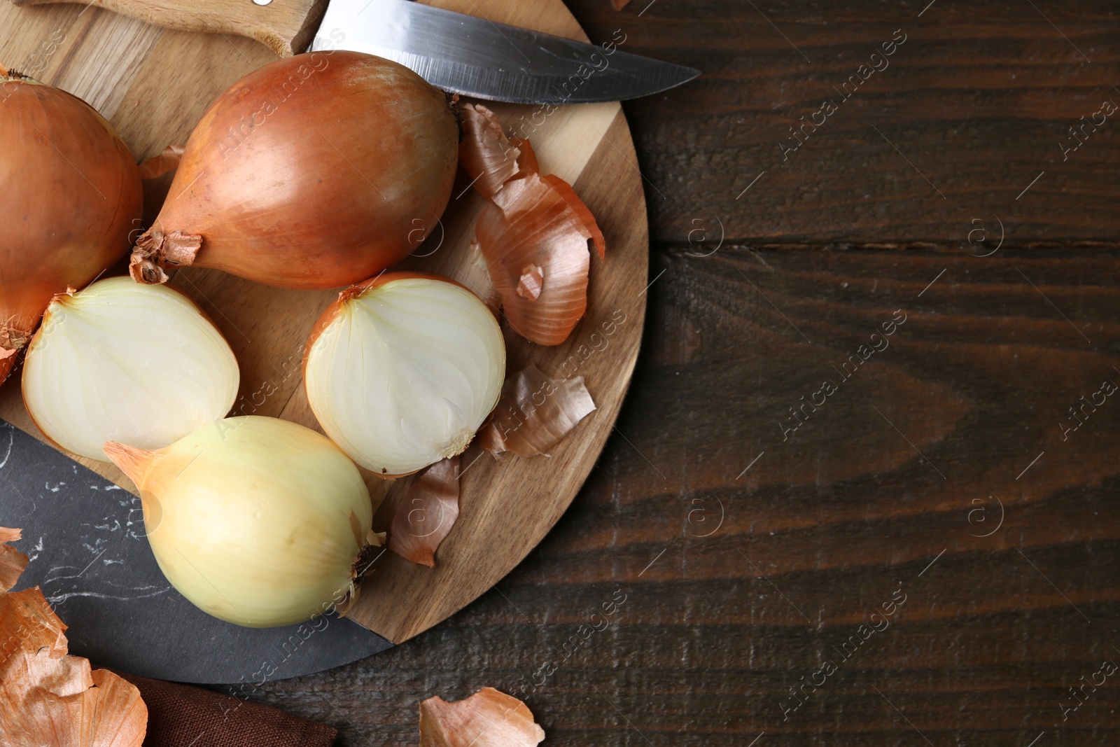 Photo of Fresh onions with peels and knife on wooden table, top view. Space for text