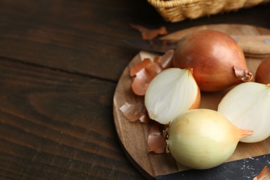 Photo of Fresh onions with peels on wooden table, closeup. Space for text