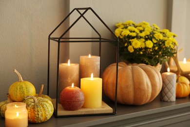 Photo of Different burning candles and pumpkins on shelf indoors. Autumn atmosphere