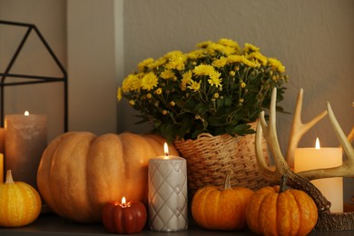 Photo of Different burning candles, flowers and pumpkins on shelf indoors. Autumn atmosphere