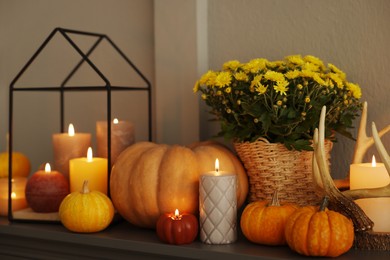 Photo of Different burning candles, flowers and pumpkins on shelf indoors. Autumn atmosphere