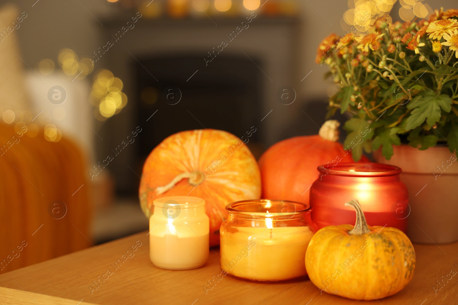 Photo of Burning candles, pumpkins and flowers on wooden table indoors. Autumn atmosphere