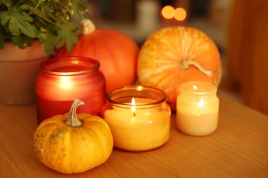 Photo of Burning candles and pumpkins on wooden table, closeup. Autumn atmosphere