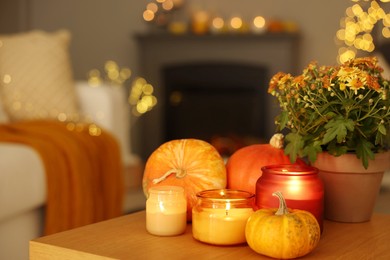 Photo of Burning candles, pumpkins and flowers on wooden table indoors, space for text. Autumn atmosphere