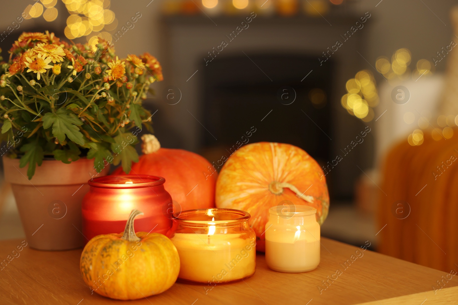 Photo of Burning candles, pumpkins and flowers on wooden table indoors. Autumn atmosphere