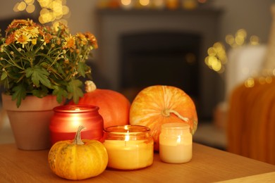 Photo of Burning candles, pumpkins and flowers on wooden table indoors. Autumn atmosphere