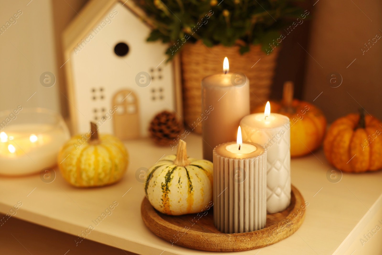 Photo of Burning candles, pumpkins and autumn decor on white table