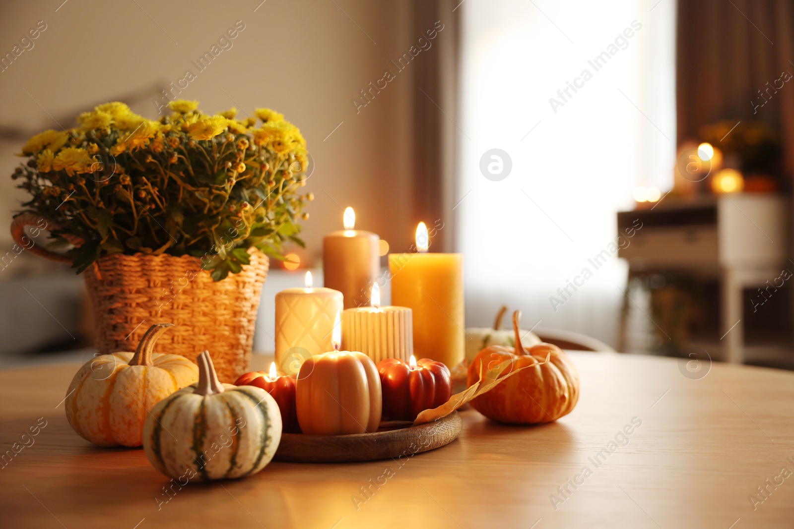 Photo of Burning candles, pumpkins and flowers on wooden table indoors. Space for text